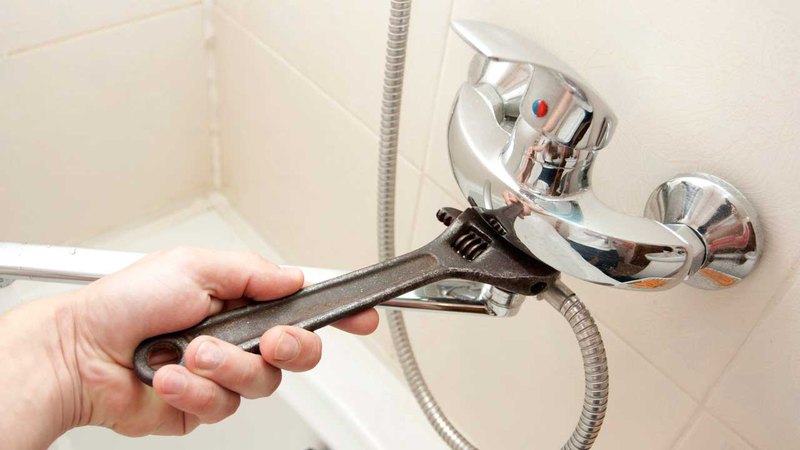 Man using an adjustable key for proper shower tub repair in case of leaking pipes